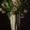 "Soft pink flowers in a textured cream vase against a dark background, showcasing delicate hues and organic shapes."