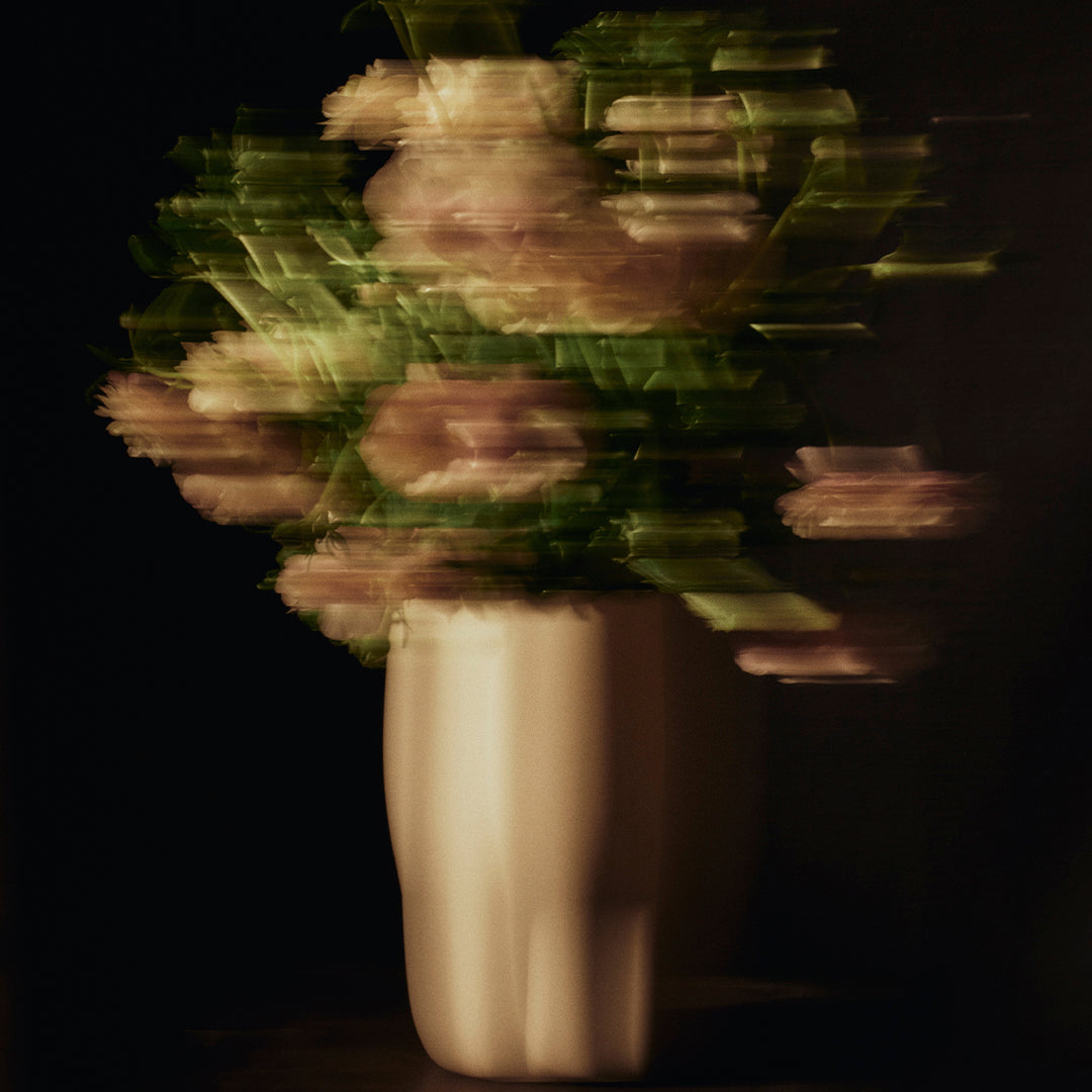 Blurred bouquet of soft pink flowers in a sleek white vase against a dark background. Elegant and artistic design.