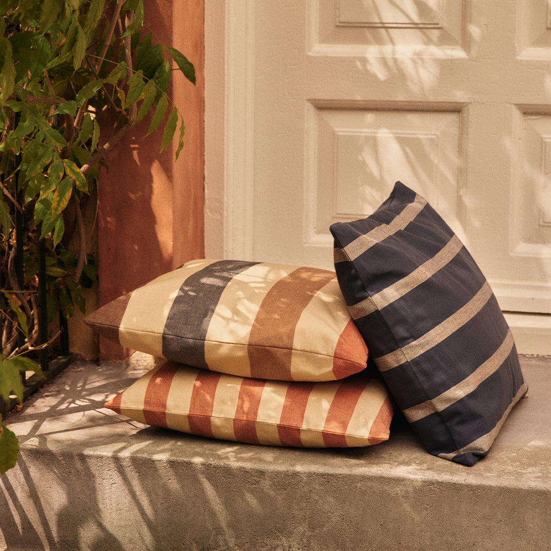 Striped decorative pillows in earthy tones of terracotta, cream, and navy blue, stacked on a concrete surface.