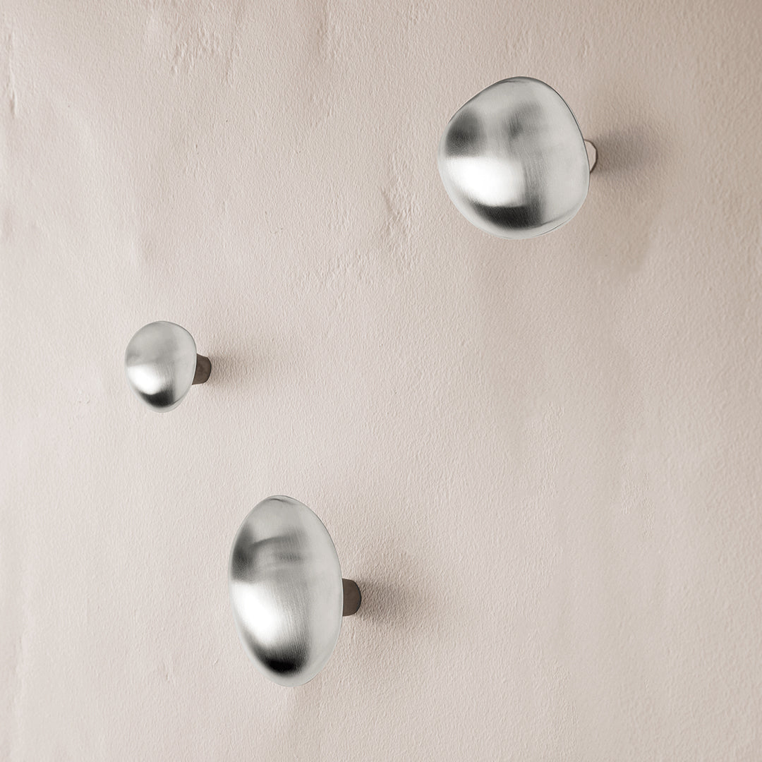Silver wall hooks with a smooth, shiny finish, featuring three different sizes against a textured light background.