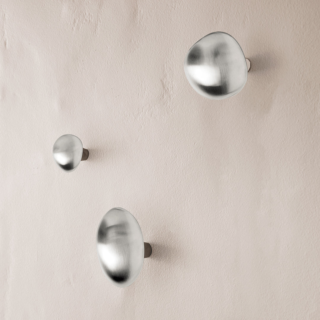 Set of three silver metallic wall hooks displaying a sleek, modern design on a light-colored background.