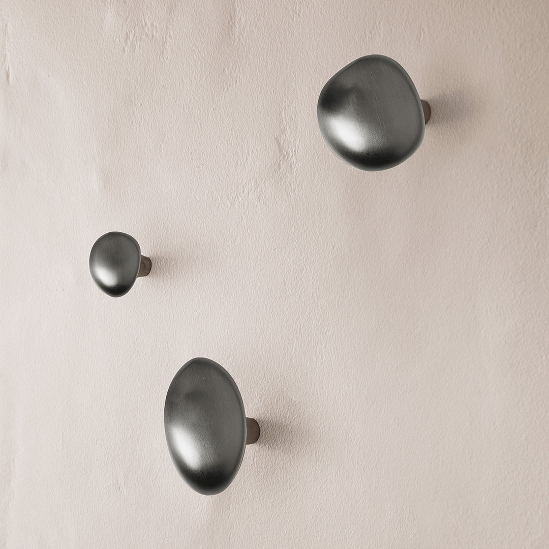 Set of three minimalist black wall hooks on a textured beige background, featuring smooth, rounded shapes.