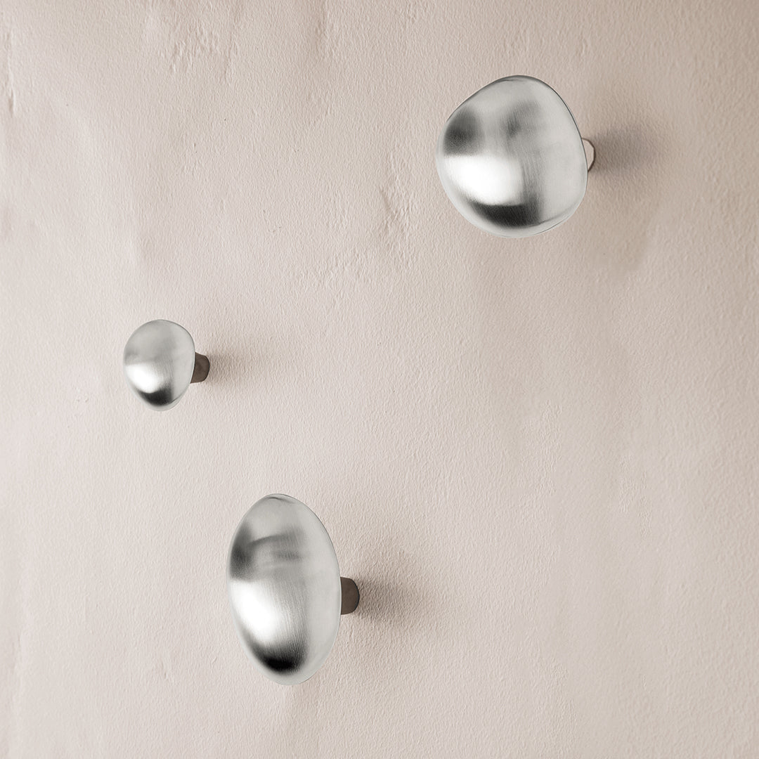 Set of three brushed silver wall hooks with smooth, rounded shapes against a soft, neutral background.