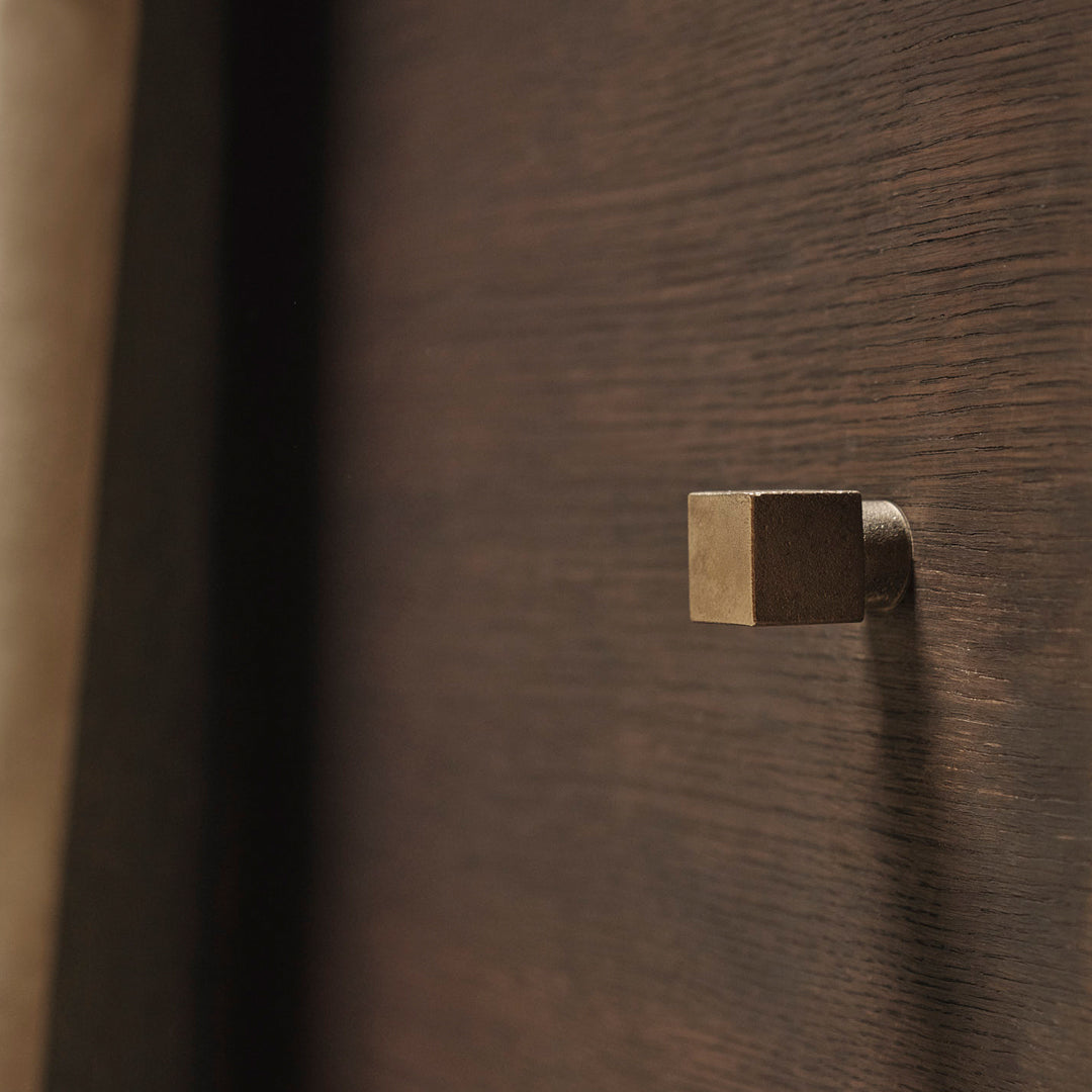 Brushed brass hook on a rich, dark wood background with subtle grain pattern. Elegant and modern design element.