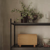 Light wood box with clean lines and natural finish, surrounded by deep brown ceramic vases and greenery accents.