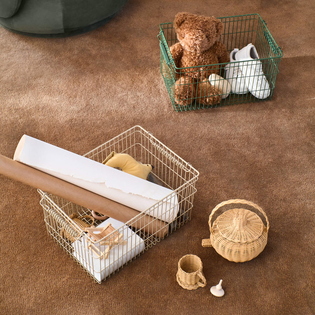 "Metal wire storage baskets in green and white, surrounded by neutral-toned decor on a brown rug."