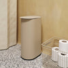 Beige cylindrical trash can with a sleek lid, set against a textured speckled floor and warm yellow wall.