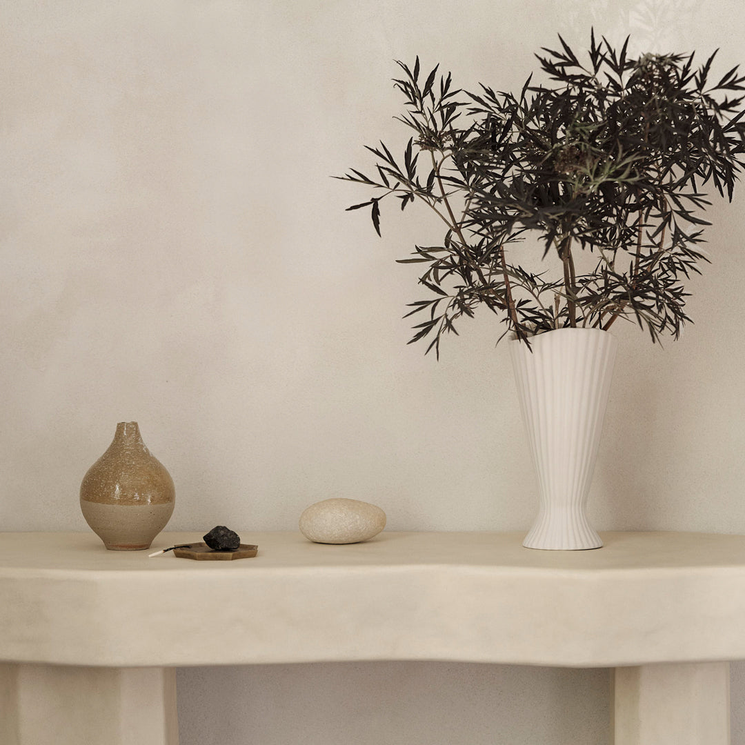 "Minimalist white vase with olive branches, earthy-toned pottery, and smooth, neutral backdrop create a calming decor."