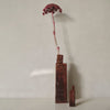 "Two geometric vases in rich brown tones with a striking pink dried flower stem, set against a neutral background."