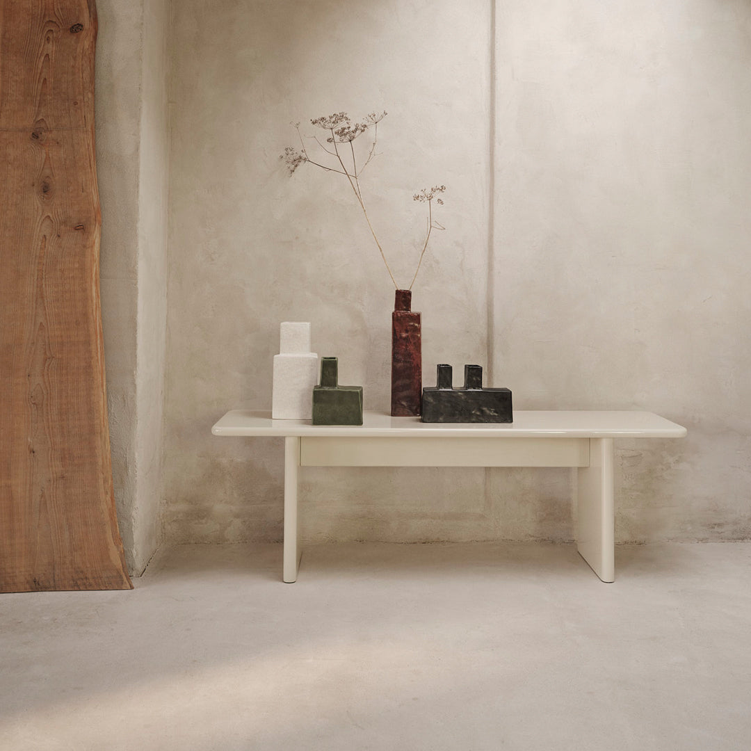 Minimalist table with neutral tones, featuring white, green, and dark red geometric vases on a textured gray backdrop.