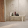 Minimalist table with neutral tones, featuring white, green, and dark red geometric vases on a textured gray backdrop.