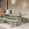 Modern green dining table and benches with a sleek, glossy surface, set against a textured stone wall backdrop.