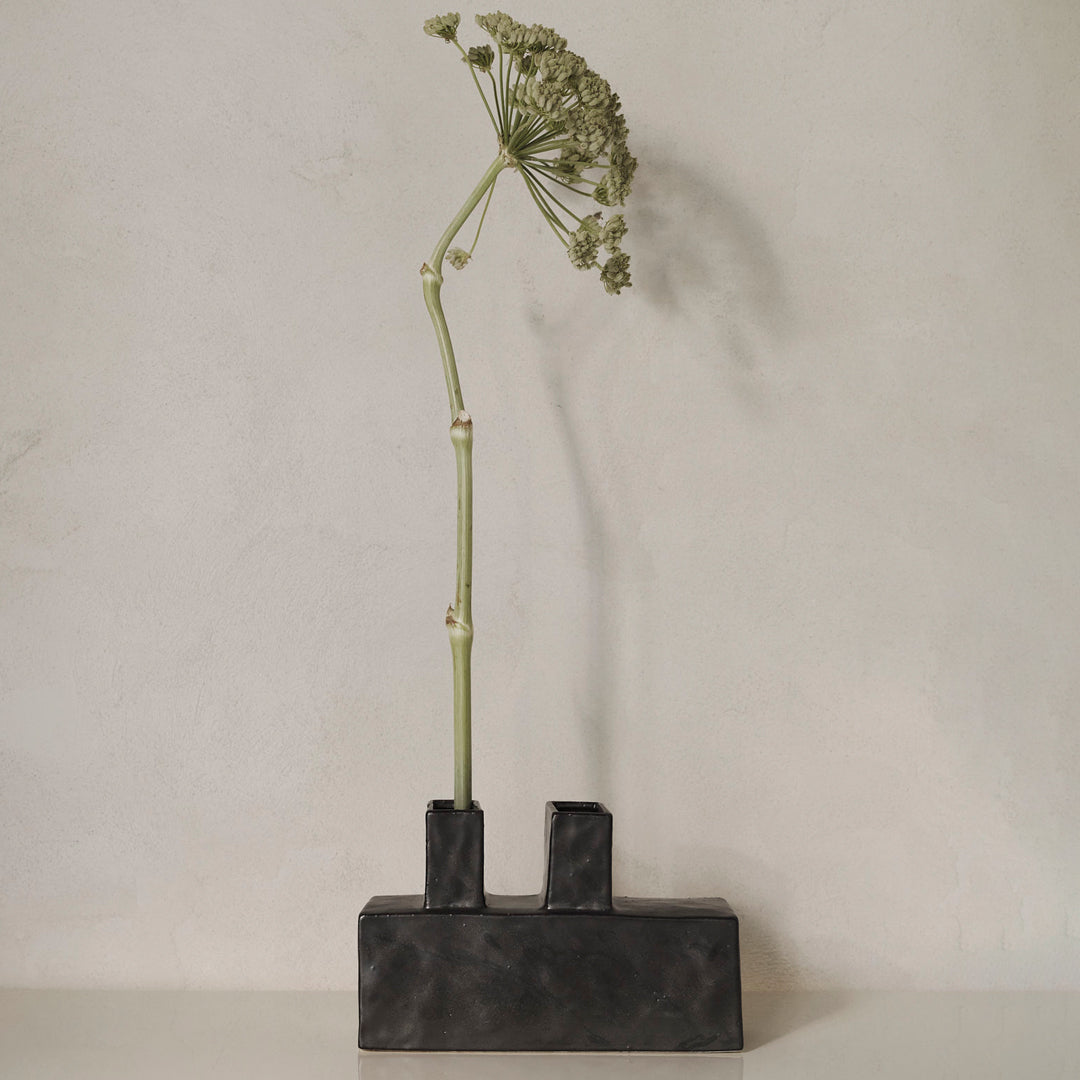 Modern black concrete vase with a sleek design, showcasing a minimalist aesthetic and natural green floral accents.