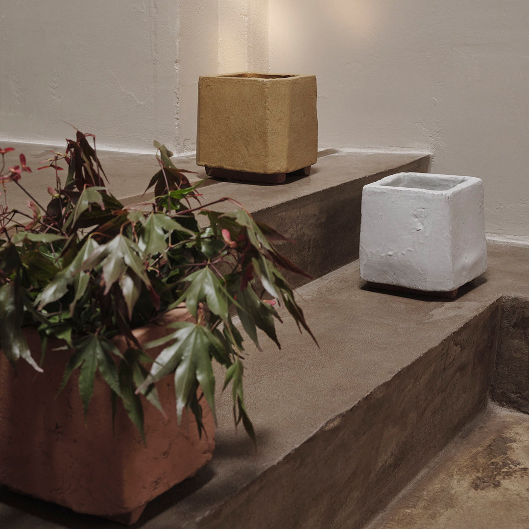 "Textured clay planters in earthy tones: terracotta, beige, and white, displayed on a minimalist concrete staircase."