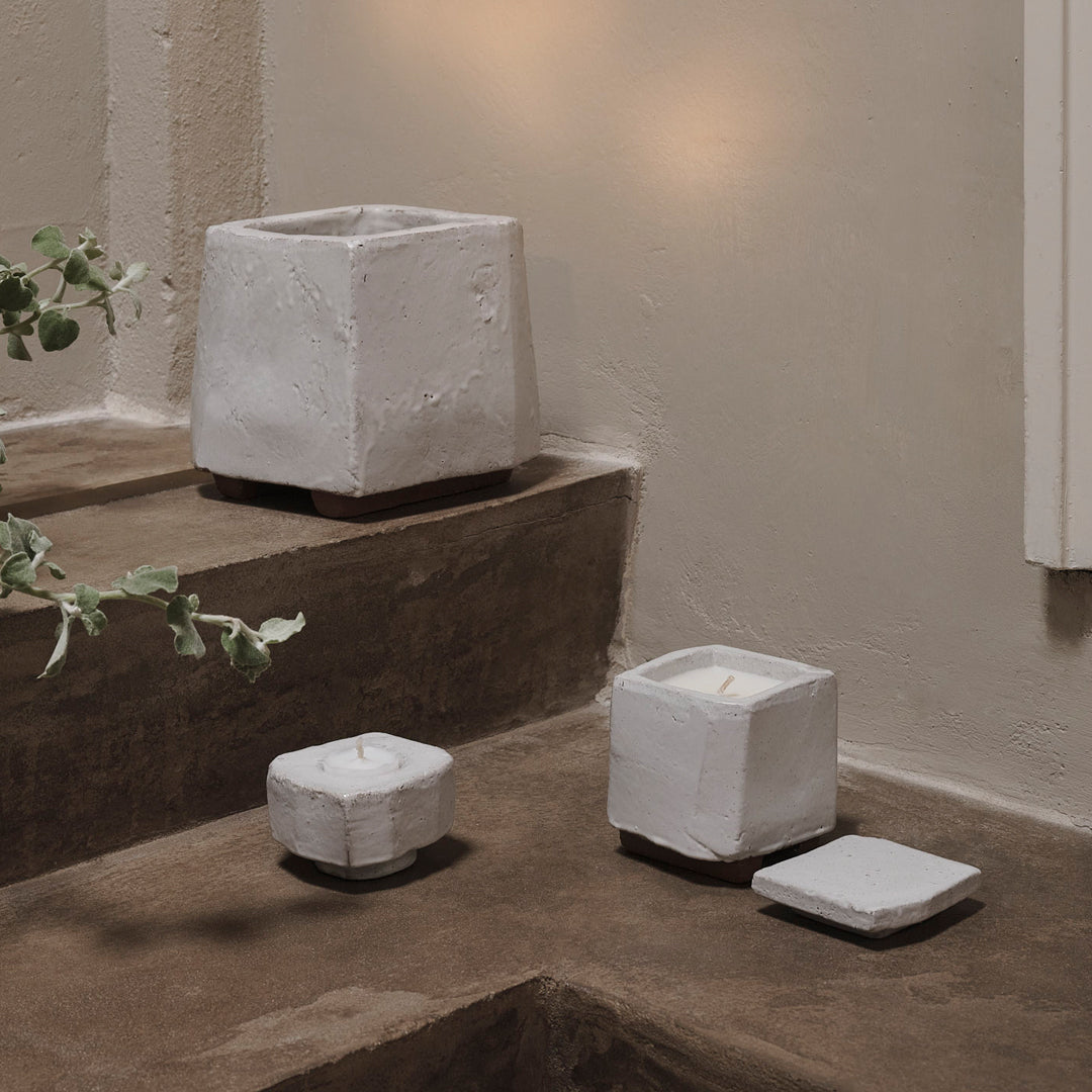 Set of textured white concrete candle holders with minimalist square designs on a rustic brown background.