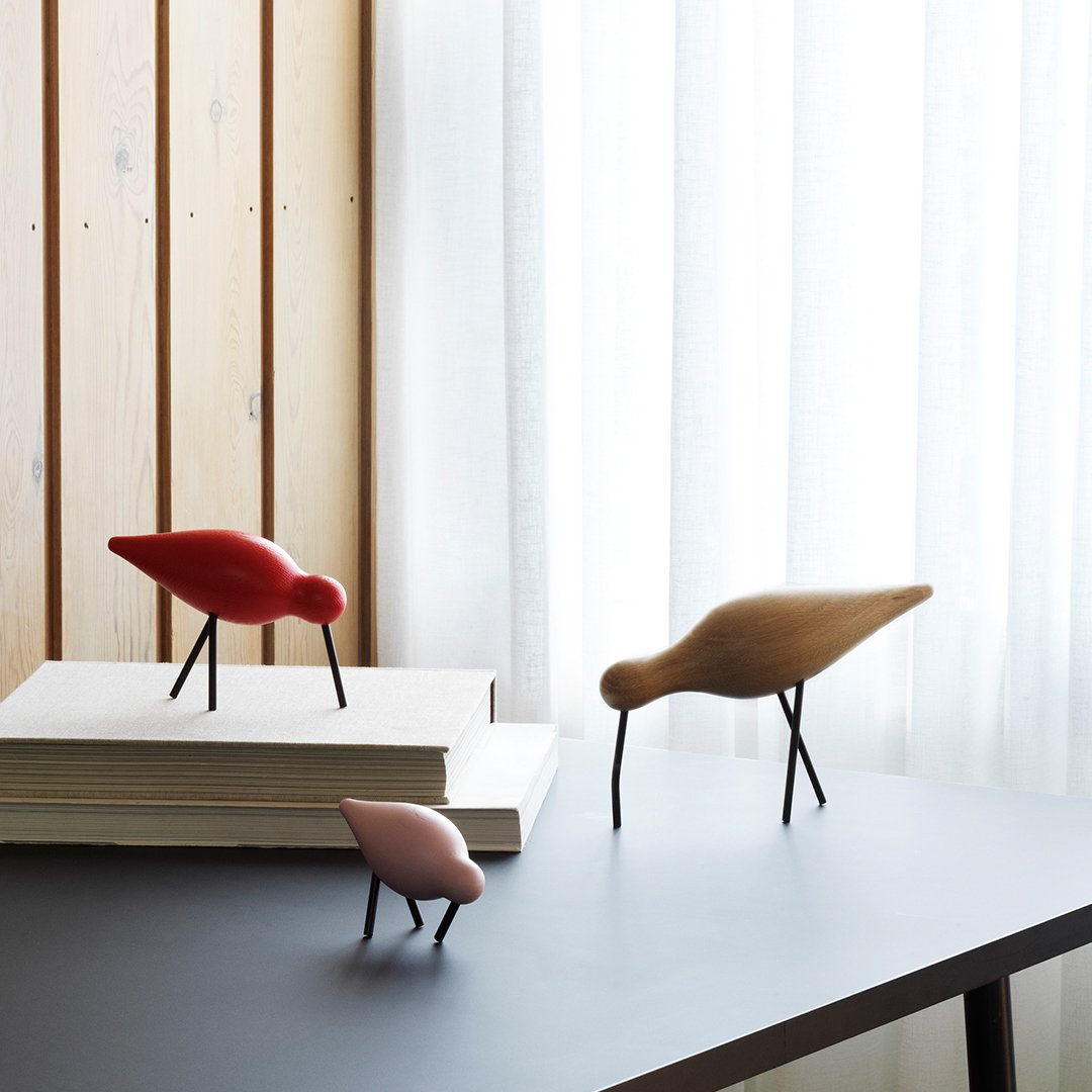"Red, pink, and brown decorative bird figurines with black legs on a modern tabletop and a wooden background."