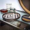 Geometric patterned serving trays in black, natural wood, and muted colors on a glass surface. Stylish home decor accent.