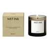 Sleek black candle with warm amber glass and minimalist beige packaging featuring black text.