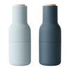 Two matte finish bottle-shaped containers in light blue and dark gray, featuring wooden lids. Modern and minimalist design.