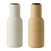 Pair of minimalist bottle-shaped containers in matte white and soft beige with brown lids.
