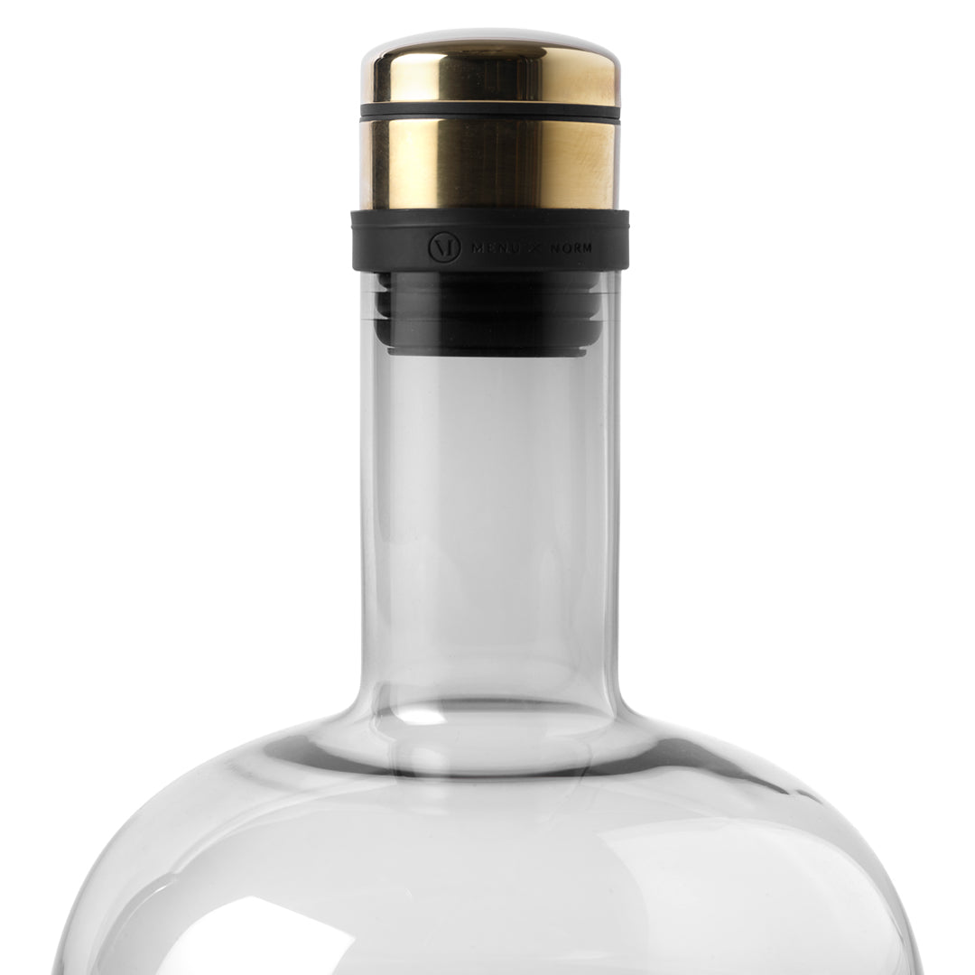 Clear glass bottle with a sleek black and gold cap, featuring a minimalist design. 