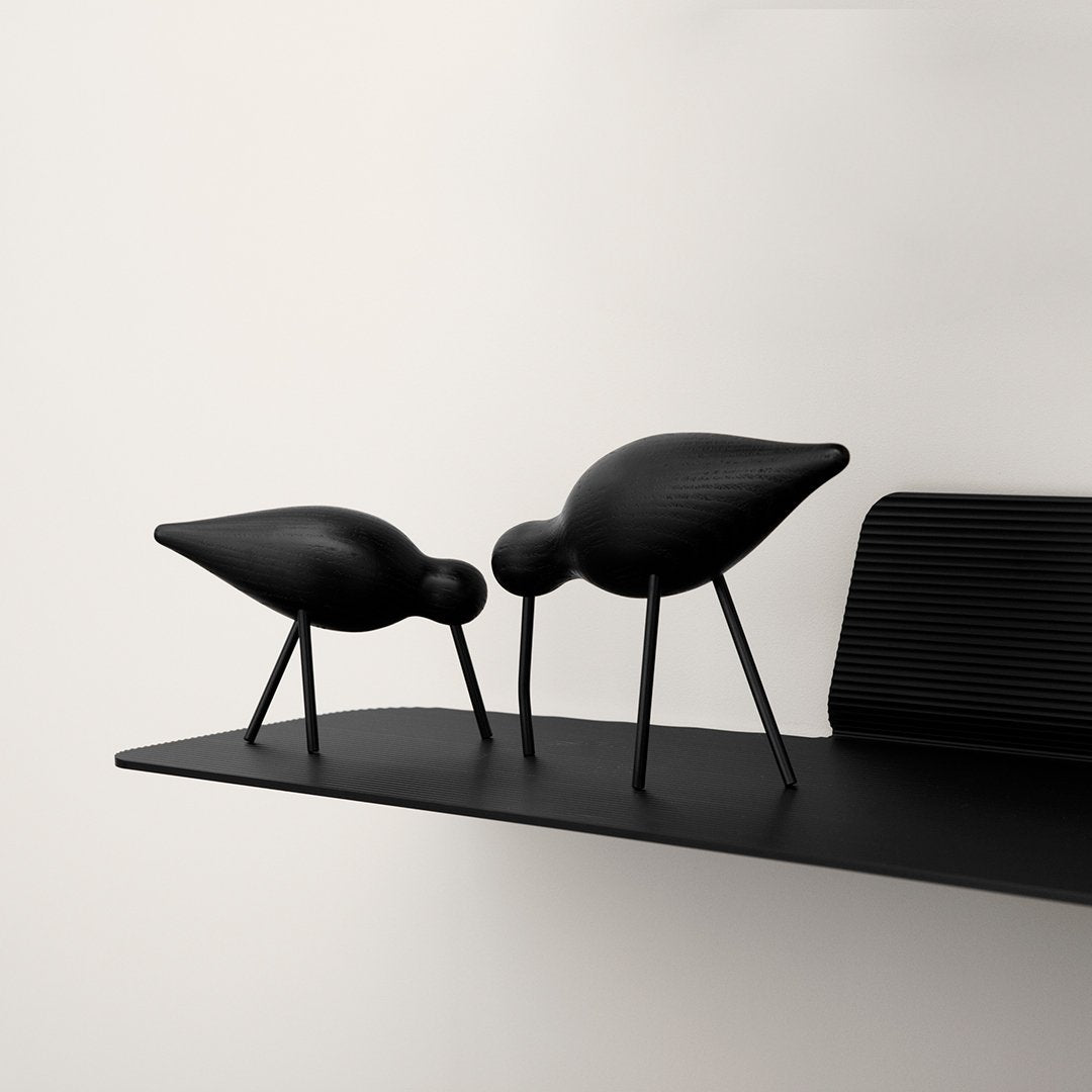 Two sleek black decorative birds on a minimalist black shelf, featuring smooth curves and subtle textures.