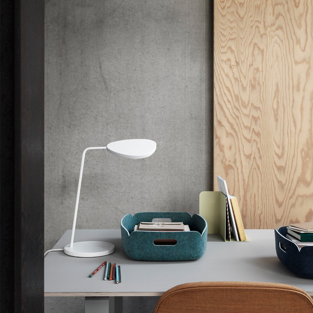 Modern white desk lamp with teal storage basket, gray tabletop, and natural wood backdrop. Clean, minimalist design.