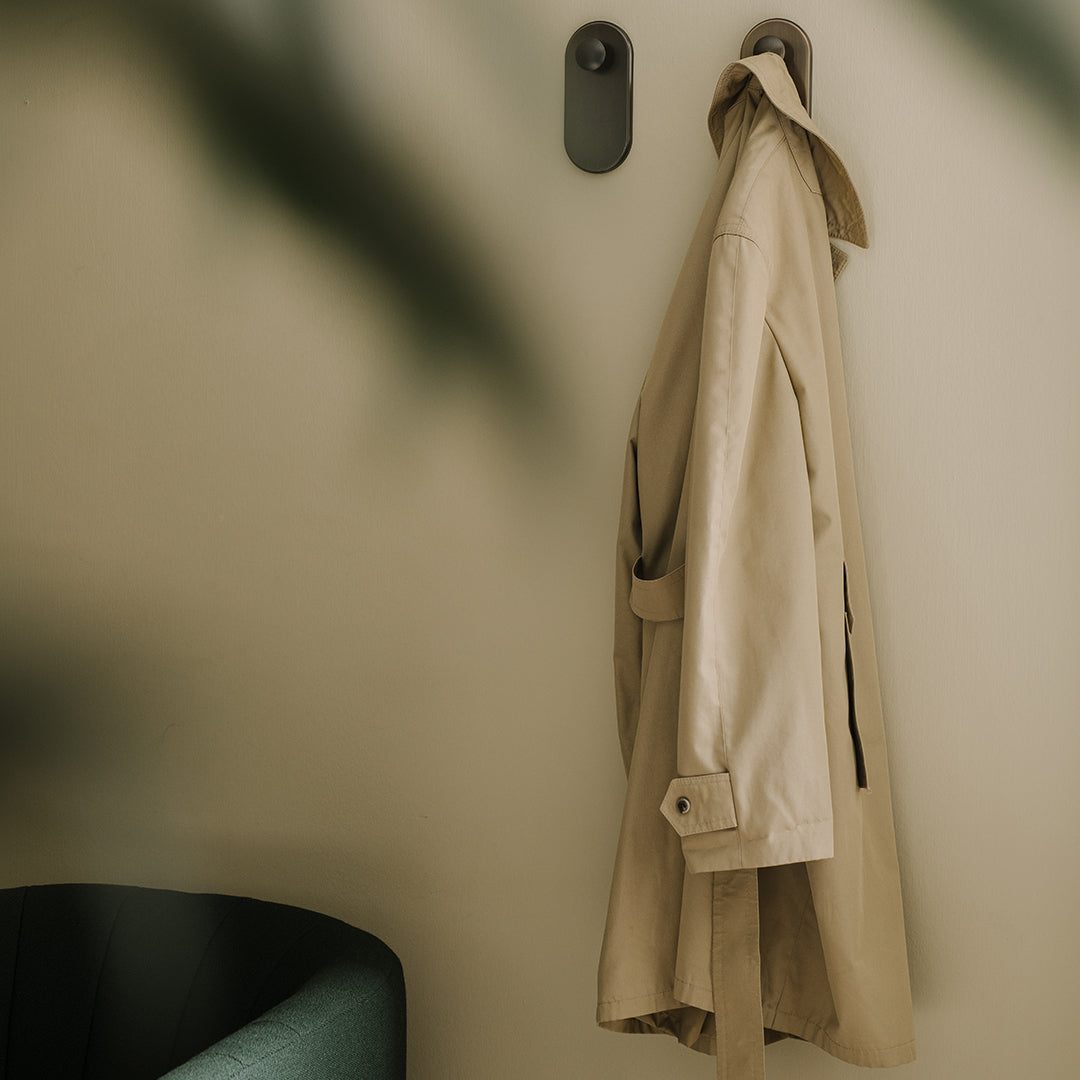 Beige trench coat hanging on a wall, complemented by a soft green accent chair and neutral background.