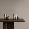 Set of textured ceramic vases in beige, gray, white, and black, displayed on a wooden table against a neutral wall.