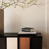 Black, white, and earthy brown bookshelf with minimalistic design and textured patterns; topped with stacked books.
