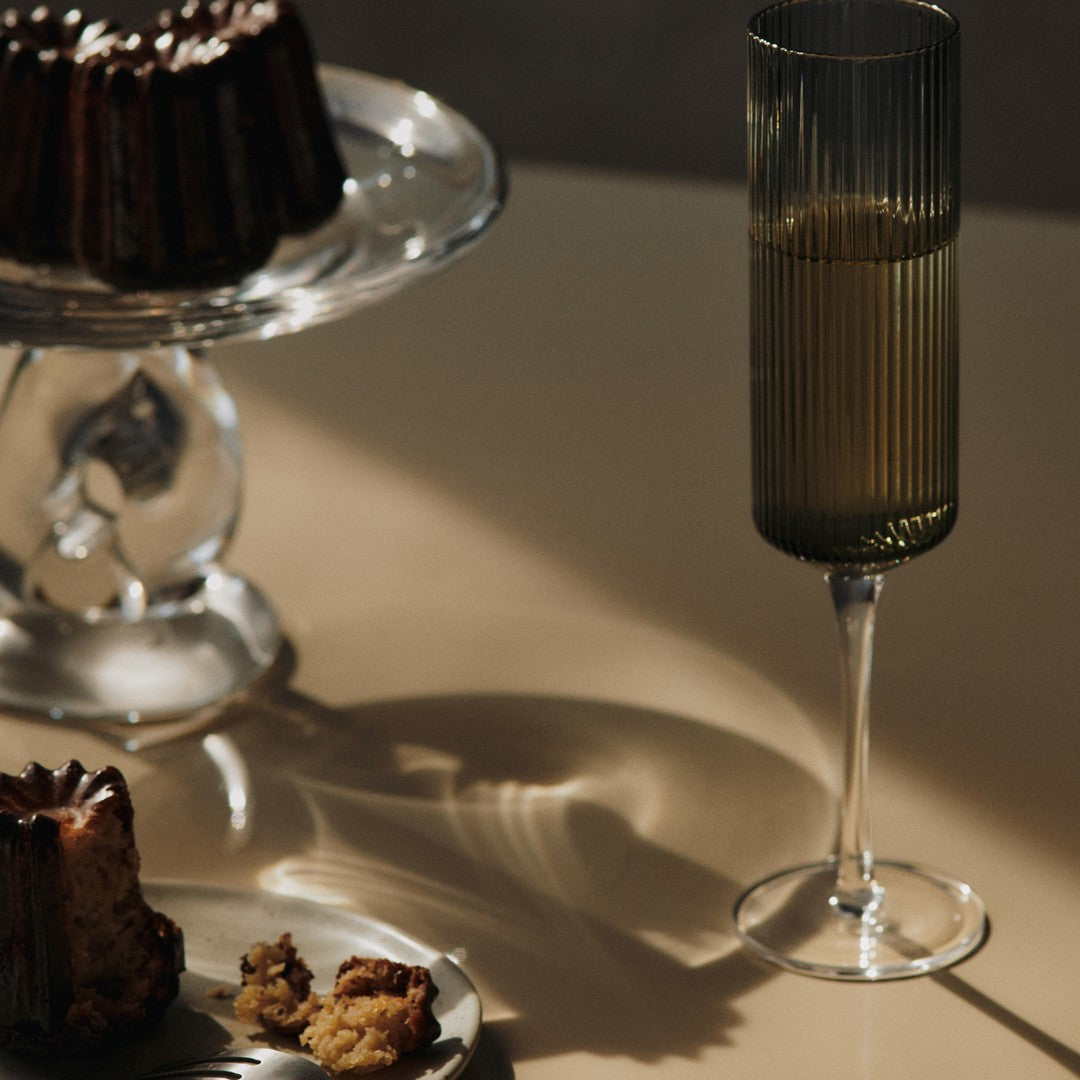 "Elegant green ribbed glass with shadows, accompanied by a rich brown cake and a neutral plate against a soft backdrop."