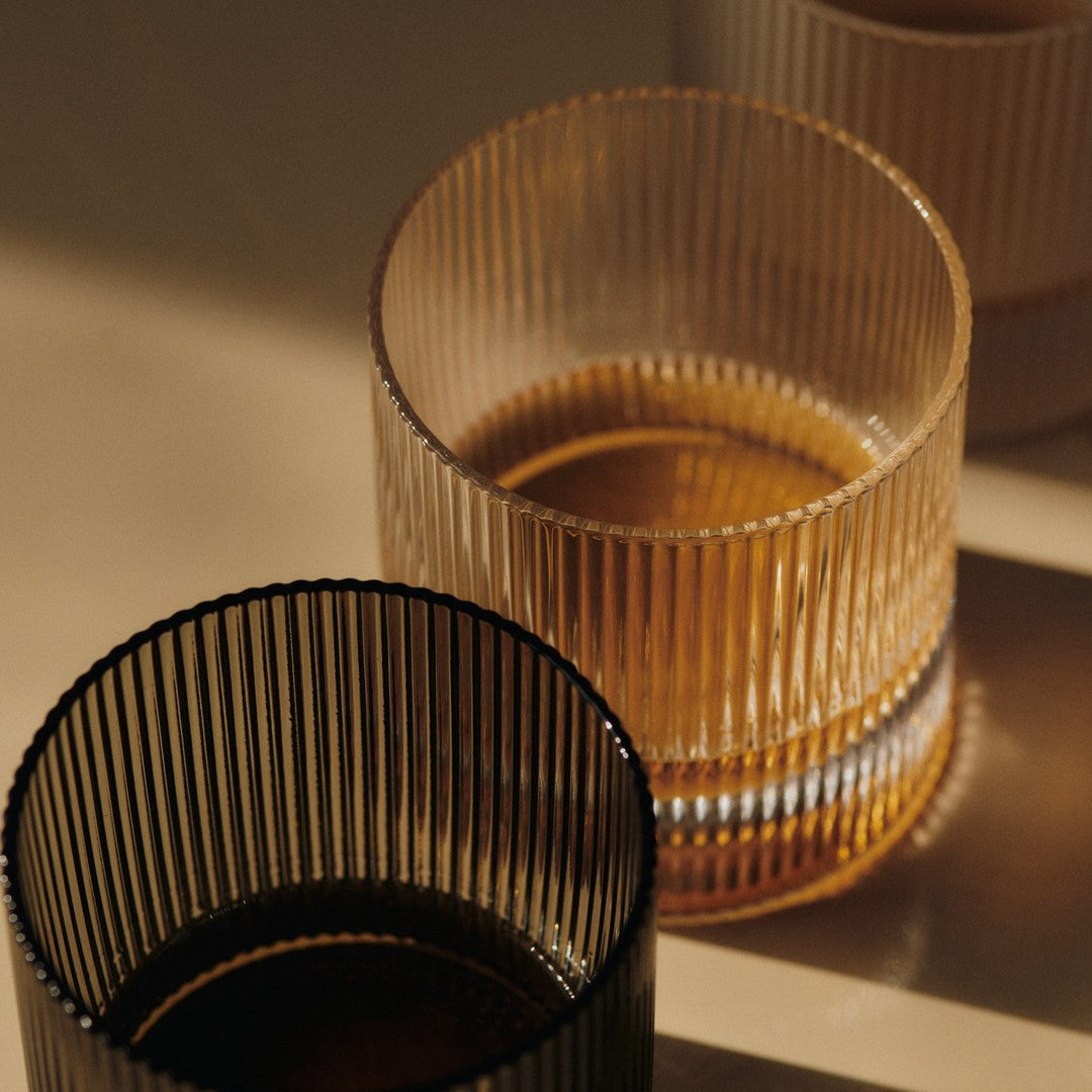Black and amber ribbed glass cups stacked on a soft beige surface with subtle reflections. Elegant and modern design.