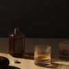 Amber whiskey in textured glass, golden rim, shadows on a neutral surface, minimalist dark background.