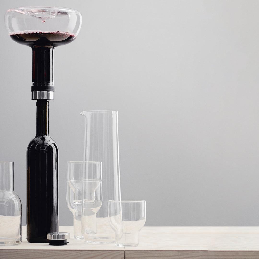 Black wine decanter with clear glassware on a light wood surface and soft grey background. Elegant and modern design.