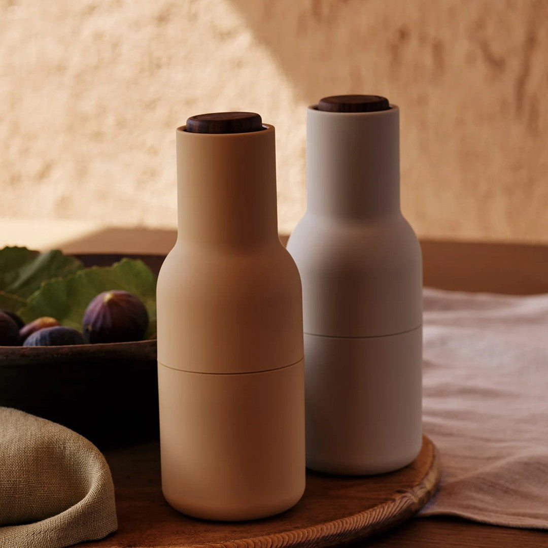 Tan and light gray bottle-shaped containers with rounded tops, arranged on a wooden tray with green leaves.