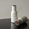 White ceramic bottles with smooth textures and wooden cork lids on a dark surface. Minimalist design with subtle colors.