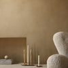 "Neutral beige wall with textured finish, soft white chair, and elegant golden candle holders, creating a warm ambiance."