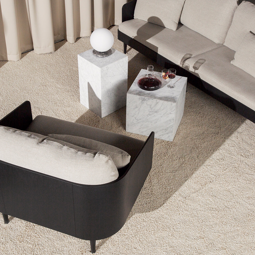 Stylish black and beige modern sofa with geometric white and gray side tables on a textured cream rug.