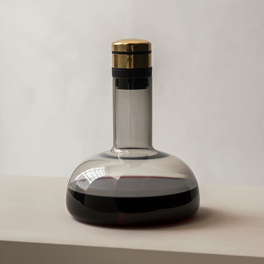 Elegant glass carafe with a sleek gray body, dark red wine, and a gold and black cap. Modern minimalist design.