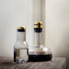 Clear glass bottles with gold and black accents, one containing water and the other red wine, on a rustic wooden surface.