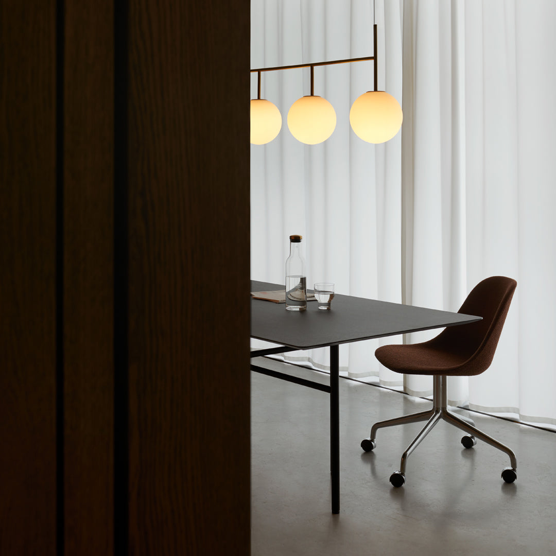Modern office interior featuring a sleek black table, brown chair, and round white pendant lights against white curtains.