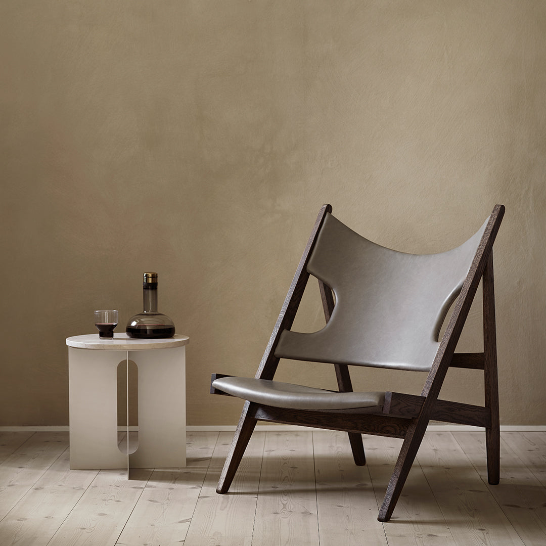 Gray leather chair with a dark wooden frame, set against a neutral beige wall, paired with a minimalist white side table.