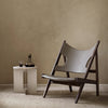 Gray leather chair with a dark wooden frame, set against a neutral beige wall, paired with a minimalist white side table.