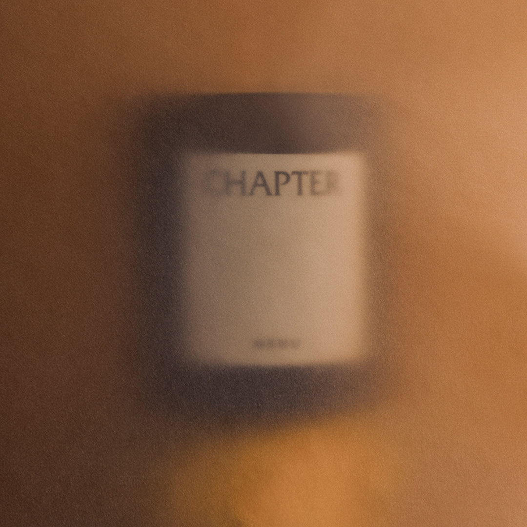Blurry candle with a black label, set against warm amber tones and soft gradients.