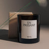 Black candle with a minimalist label, set against soft beige and gray tones, featuring subtle green accents.