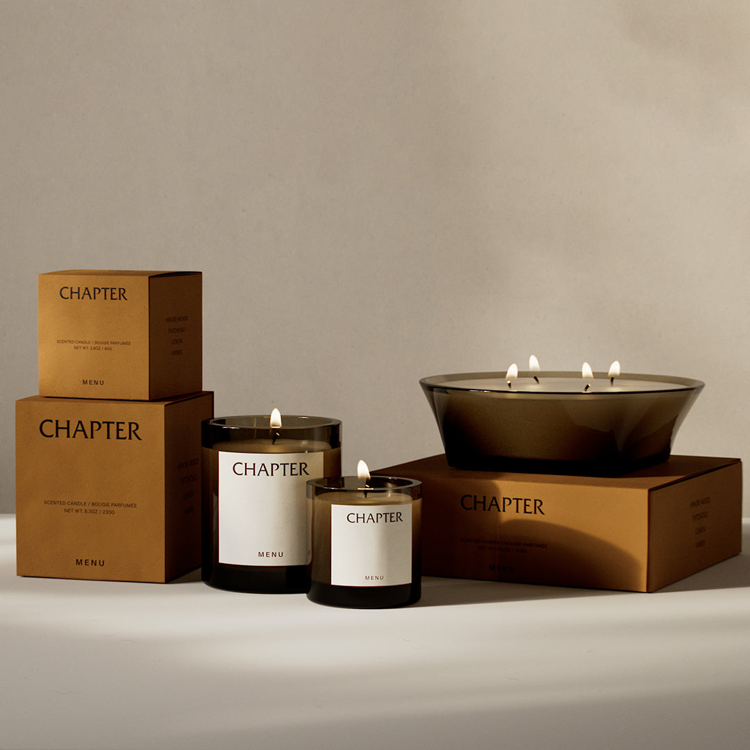 Elegant brown and black candle packaging with minimalist white labels and warm, flickering candlelight accents.