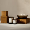 Elegant brown and black candle packaging with minimalist white labels and warm, flickering candlelight accents.