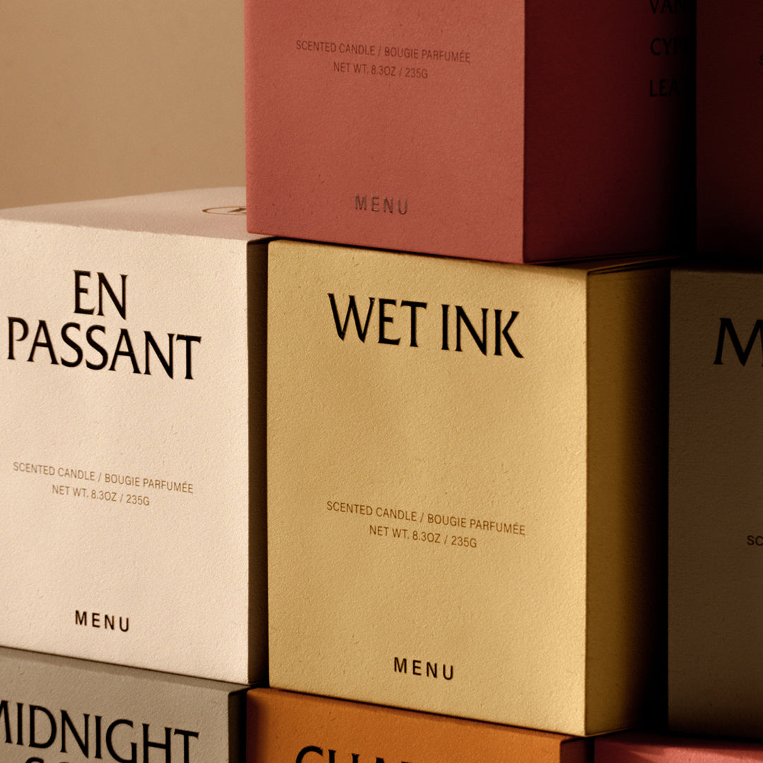 Colorful candle packaging featuring soft pink, golden, beige, and earthy tones with bold black text.