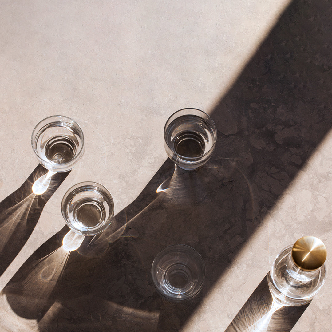 "Clear glass cups casting shadows on a textured, light gray surface with a hint of golden metal accents."