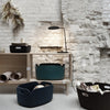 Black, dark teal, and navy felt storage baskets with curved edges against a textured white brick background.